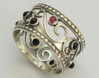 May include: A silver ring with a delicate filigree design and five gemstones. The ring has a beaded edge and features two pink and three black gemstones.