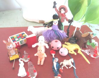 Puede incluir: Una colección de figuras en miniatura que incluye un conejo marrón en un carrito amarillo, una oveja blanca, una muñeca con pelo de lana morado, un caballo marrón, un caballo blanco pequeño, un muñeco bebé, un carrito rojo y blanco y abalorios.