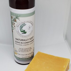 以下が含まれることがあります： 「NATURALLY SOFT LEAVE-IN CONDITIONER」と書かれた茶色のボトルと黄色のバー。ボトルは黒いキャップとテキストと植物のイラストが入ったラベルが付いています。バーは長方形です。