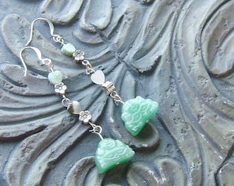 May include: A pair of silver earrings with green jade-like pendants. The pendants are carved with intricate designs and have a floral motif. The earrings are strung with silver beads and a white heart-shaped bead.