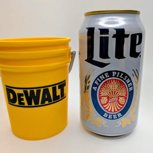 May include: A yellow DEWALT bucket with a silver handle next to a silver Lite beer can. The beer can has a gold top and a circular emblem with the words "A Fine Pilsner Beer".