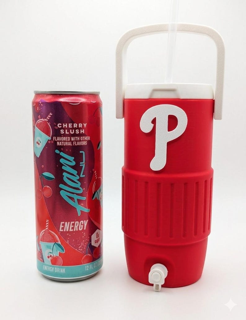 May include: A 12 fluid ounce Alani Nu Cherry Slush energy drink can next to a red insulated beverage cooler with a white handle, a white spigot at the base, and a large white letter P emblem on the front, featuring a clear straw extending from the top.