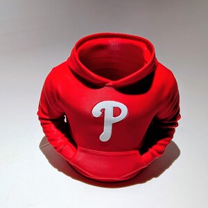 May include: A red hoodie-shaped planter with a white "P" logo on the front. The planter has a hood and two front pockets. The design is a 3D-printed item, perfect for small plants or as a decorative piece.