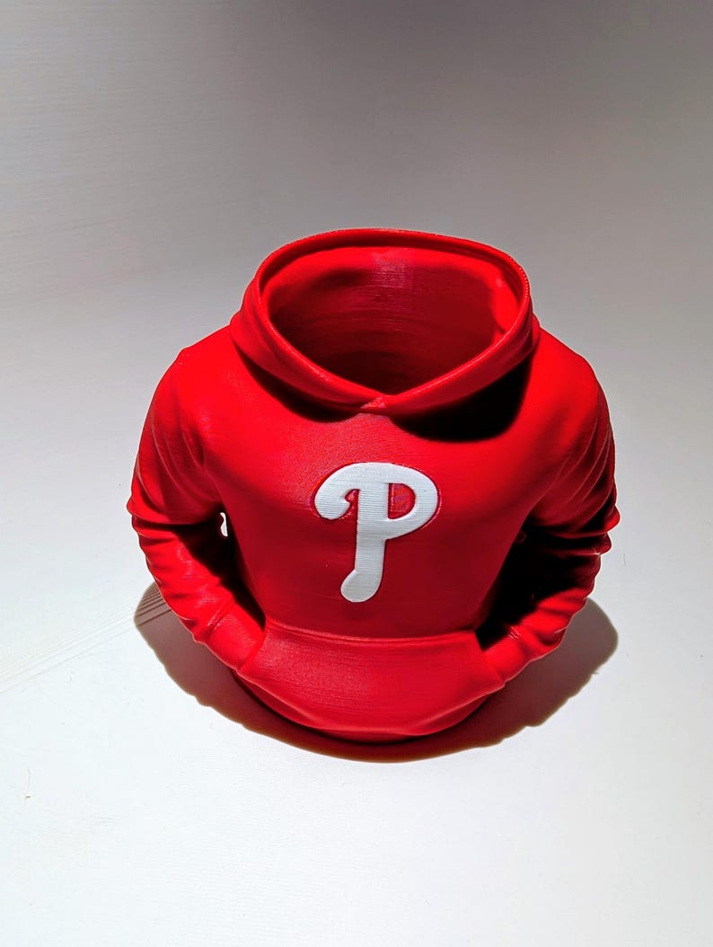 May include: A red hoodie-shaped planter with a white "P" logo on the front. The planter has a hood and two front pockets. The design is a 3D-printed item, perfect for small plants or as a decorative piece.