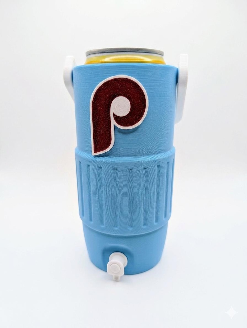 May include: A light blue beverage cooler with a white handle and a white spigot at the base. The front features a large, maroon and white letter P logo with a textured, glittery finish. A yellow and silver beverage can is inserted at the top.