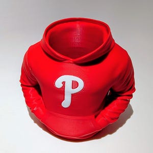 May include: A red hoodie-shaped decorative item with a white "P" logo on the front. The item has a hood, sleeves, and a pocket area. The object is likely a decorative piece or a container, possibly for holding small items.