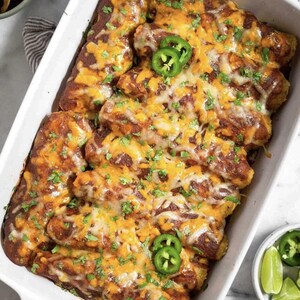 A white casserole dish filled with a cheesy enchilada casserole, topped with jalapenos and garnished with cilantro.