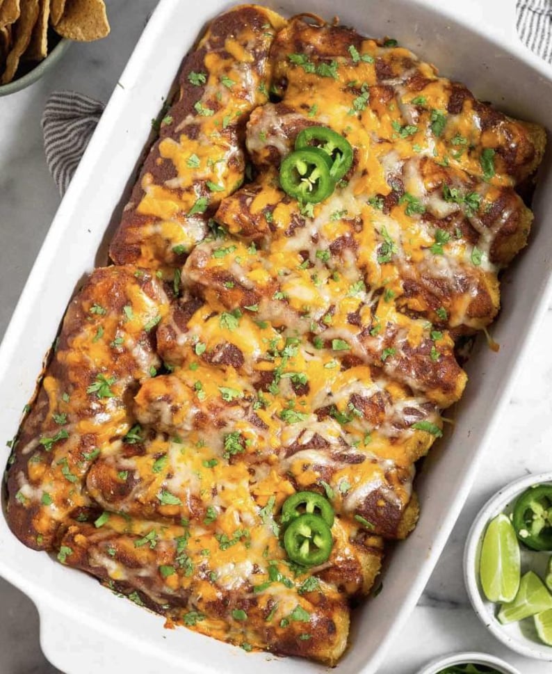 A white casserole dish filled with a cheesy enchilada casserole, topped with jalapenos and garnished with cilantro.