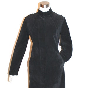 May include: A black suede coat with a high collar and long sleeves. The coat has a button-down front and two pockets. The coat is displayed on a mannequin against a white background. The coat is knee-length.