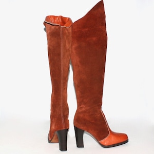 May include: A pair of knee-high boots in shades of brown and orange. The boots have a suede-like texture, with a darker brown heel and a lighter orange toe. The interior lining is a bright orange.