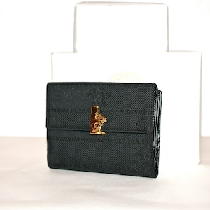 May include: Black wallet with a textured pattern and a gold-colored Medusa head clasp. The wallet has a rectangular shape and a fold-over design. The background includes a white box.