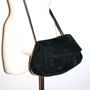May include: A black suede crossbody bag with a flap closure and a long, thin strap. The bag is displayed on a mannequin and has a small, decorative detail on the front.