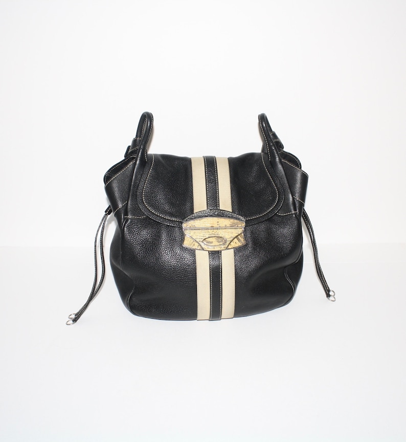 Pu&ograve; includere: Borsa in pelle nera con una striscia beige al centro e una chiusura decorativa. La borsa ha due manici e chiusure con coulisse su ogni lato. La borsa &egrave; su sfondo bianco.