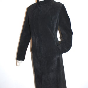 May include: A black suede coat with a high collar and long sleeves. The coat has a tailored fit and a knee-length hem. The coat is displayed on a mannequin against a white background. The coat has two pockets.