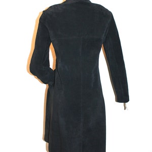 May include: A black suede coat with a high collar and long sleeves. The coat is knee-length and has a tailored fit. The back of the coat is visible, showing the seams and the overall shape. The coat is displayed on a mannequin.