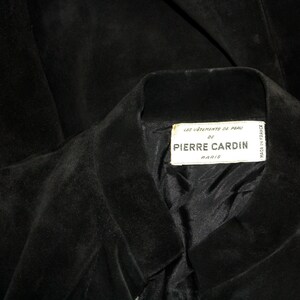 May include: Close-up of a black suede jacket with a notched collar. The label reads "LES VETEMENTS DE PEAU DE PIERRE CARDIN PARIS". The jacket's interior lining is visible.