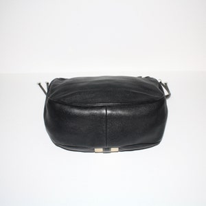 Pu&ograve; includere: Una borsa in pelle nera dalla forma arrotondata. La borsa ha una texture liscia e dettagli argentati sulla base. La borsa ha una tracolla e una chiusura con coulisse.