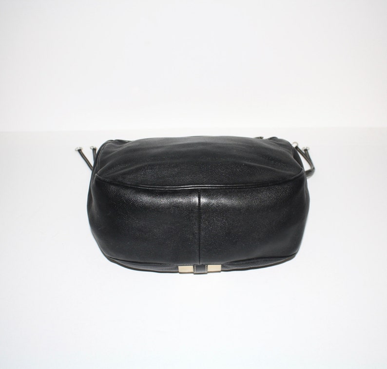 Pu&ograve; includere: Una borsa in pelle nera dalla forma arrotondata. La borsa ha una texture liscia e dettagli argentati sulla base. La borsa ha una tracolla e una chiusura con coulisse.