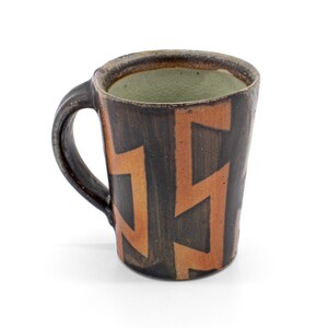 May include: A brown ceramic mug with a geometric pattern in shades of brown and orange. The mug has a handle and a wide rim.