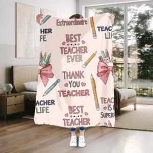 Puede incluir: Una manta rosa claro con un patrón repetido de lápices, lazos y texto. El texto incluye frases como "Mejor profesor de todos los tiempos" y "Gracias profesor". Un regalo para un profesor.