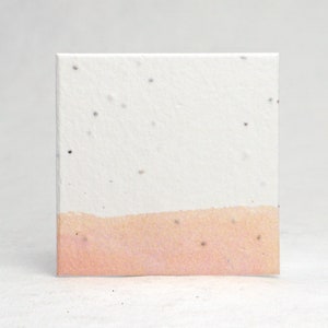 May include: A square card made of white paper with a light pink band across the bottom. The paper has small black flecks throughout.