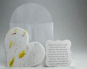 May include: A white heart-shaped seed paper with yellow and brown flower petals embedded in it. The paper is packaged in a white envelope. The instructions on the envelope read: "Plant in your garden or start it in a pot but ensure the seeds have daily watering for 4-6 weeks. The dirt should be firmed down and the seeds should not be more than 1/4 inch deep. Plant when and where 4 hours of sunlight will touch the planting each day."