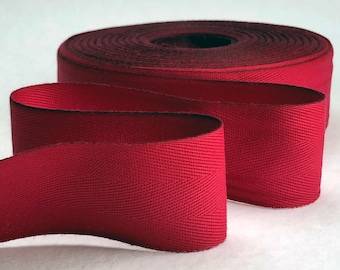 May include: A roll of red twill tape with a herringbone pattern. The tape is approximately 1 inch wide.