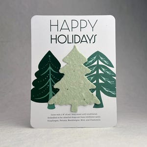 May include: A white card with the text "HAPPY HOLIDAYS" and three green Christmas tree designs. The center tree is a light green, seed-embedded shape. The card includes instructions for planting wildflower seeds.