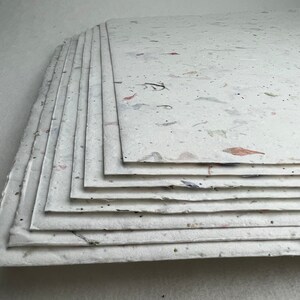 May include: A stack of white handmade paper sheets with flecks of natural materials, such as flowers and leaves, embedded in the paper.