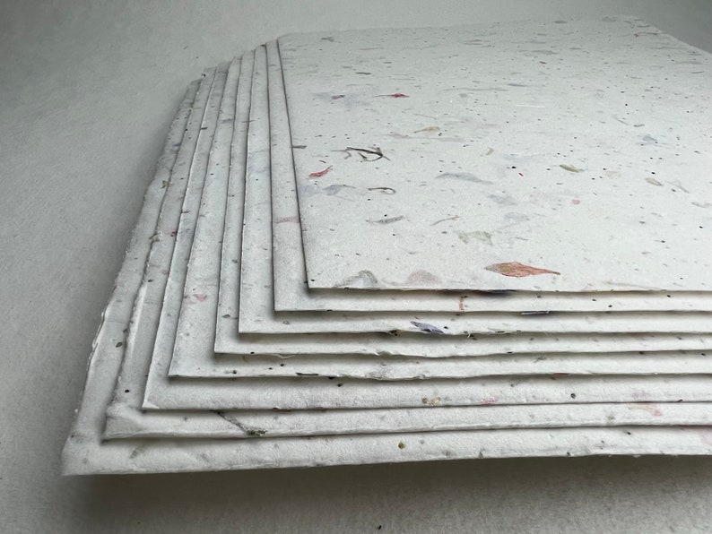 May include: A stack of white handmade paper sheets with flecks of natural materials, such as flowers and leaves, embedded in the paper.