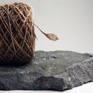 May include: A ball of brown twine with a dried leaf attached, sitting on a gray rock.