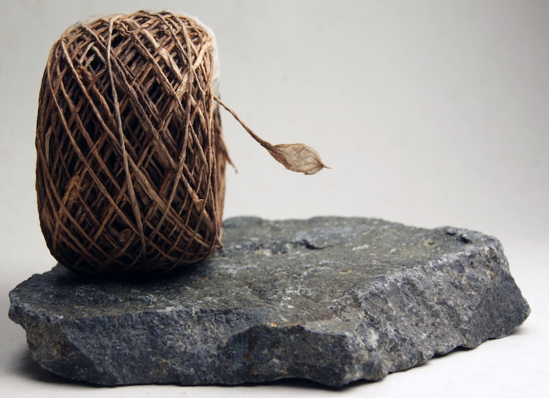 May include: A ball of brown twine with a dried leaf attached, sitting on a gray rock.