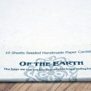 May include: A stack of 10 sheets of seeded handmade paper cardstock. The paper is white and has a natural texture. The packaging has a black and white design with the text "OF THE EARTH" and the words "The bags we use are biodegradable bopp cellophane".
