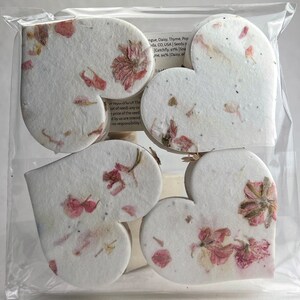以下が含まれることがあります： ピンクと白の花が押し花された、白いハート型の紙の装飾が6つ。ハートは透明なビニール袋に入っています。