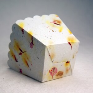 May include: A white paper box with a scalloped edge and a floral pattern. The box is made of recycled paper and has a natural, rustic look.