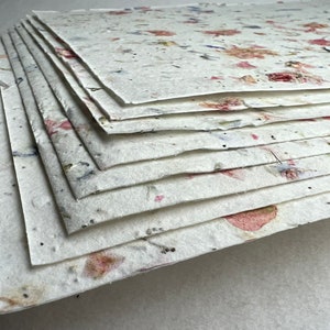 May include: A stack of handmade paper sheets with embedded flowers and petals. The paper is white with pink, red, and blue accents.