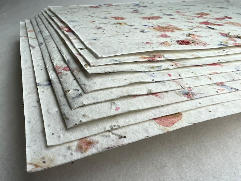 May include: A stack of handmade paper sheets with embedded flowers and petals. The paper is white with pink, red, and blue accents.
