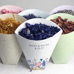 May include: A collection of five cone-shaped paper holders filled with dried flower petals in various colors including yellow, blue, pink, and purple. The front white cone features the printed text EMILY & RYLAN 8-25-27 and a floral illustration.