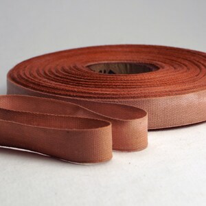 May include: A roll of brown cotton ribbon with a loose end. The ribbon is about 1 inch wide.