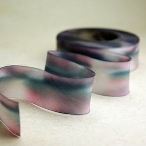 Può includere: Un primo piano di un nastro con un design simile all'acquerello in tonalità di rosa, blu e verde. Il nastro è arricciato e attorcigliato, creando un effetto dinamico e artistico.