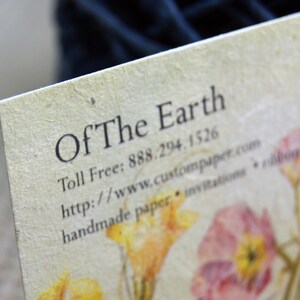 May include: A business card with the text "Of The Earth" and contact information. The card has a rustic, handmade look with a floral design.