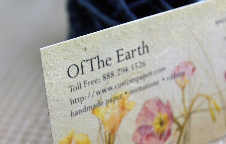 May include: A business card with the text "Of The Earth" and contact information. The card has a rustic, handmade look with a floral design.