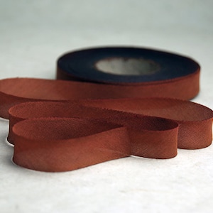 May include: A roll of dark blue tape sits behind a length of brown leather strips. The leather strips are arranged in a looping pattern, with a textured surface. The background is a light, neutral color.
