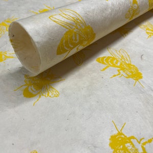 May include: A roll of white wrapping paper with a yellow bee pattern. The paper is rolled up and the end is visible.