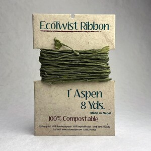 May include: A spool of green EcoTwist Ribbon wrapped around a tan paper card. The card features the text EcoTwist Ribbon, 1 inch Aspen, 8 yards, Made in Nepal, and 100% Compostable. The ribbon is a textured, twisted paper material in a deep olive green.