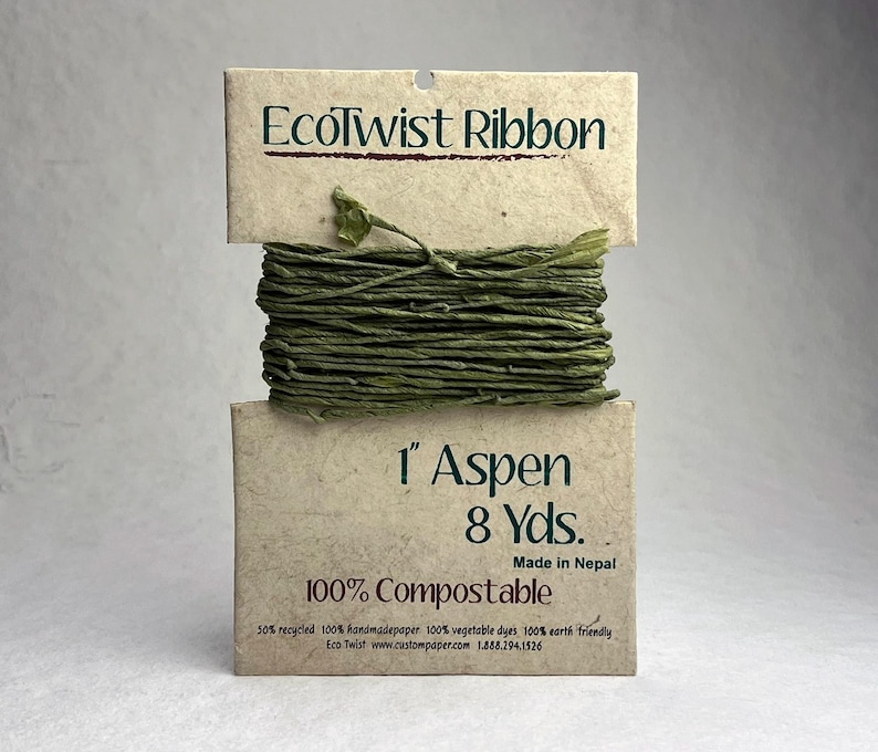 May include: A spool of green EcoTwist Ribbon wrapped around a tan paper card. The card features the text EcoTwist Ribbon, 1 inch Aspen, 8 yards, Made in Nepal, and 100% Compostable. The ribbon is a textured, twisted paper material in a deep olive green.