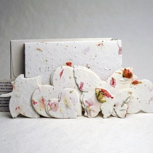 May include: A set of handmade paper decorations in the shape of hearts, butterflies, and clouds. The paper is made from recycled fibers and features embedded flower petals in shades of pink and white.