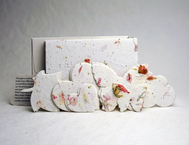May include: A set of handmade paper decorations in the shape of hearts, butterflies, and clouds. The paper is made from recycled fibers and features embedded flower petals in shades of pink and white.