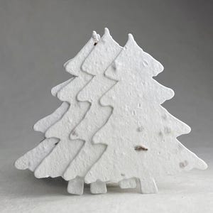 May include: Three white paper Christmas tree cutouts. The trees are layered, creating a 3D effect. The paper has a textured, speckled appearance. The trees are a festive decoration.