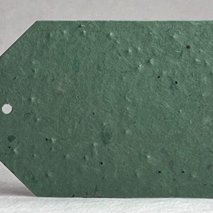 May include: A textured, green tag with a unique shape, featuring a hole for stringing. The tag's surface has a speckled appearance, adding to its rustic charm. The tag is a solid, muted green color.